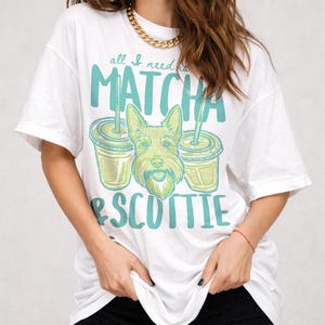 May include: White t-shirt with a graphic design featuring the text "all I need is MATCHA & SCOTTIE". The design includes two matcha drinks and a cartoon Scottish Terrier dog. The shirt is a relaxed fit.