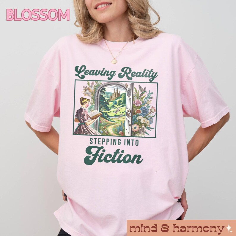 May include: Pink t-shirt with a graphic of a woman reading a book in front of a doorway with the text "Leaving Reality Stepping Into Fiction".
