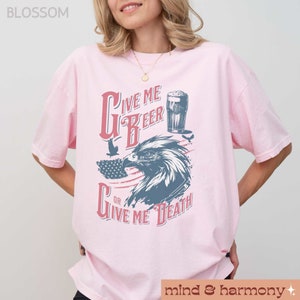 Peut inclure: T-shirt rose avec un motif graphique repr&eacute;sentant un aigle, un drapeau am&eacute;ricain et le texte "Give Me Beer or Give Me Death".