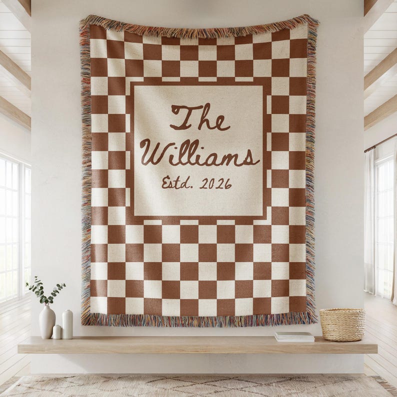 May include: A brown and cream checkered throw blanket with fringed edges. The center features a cream-colored square with the text "The Williams Estd. 2026" in a script font. The blanket is displayed on a wall.