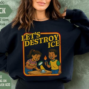 May include: Black sweatshirt with the text "LET'S DESTROY ICE" in a yellow and red frame. The graphic shows two cartoon children experimenting with ice. The sweatshirt also has the text "MIND & HARMONY GIFTS".