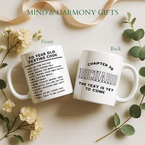 May include: Two white ceramic mugs with black text. One mug says "70 YEAR OLD TEXTING CODE" with abbreviations and their meanings. The other mug says "CHAPTER 70 RICHARD THE TEXT IS YET TO COME". The mugs are surrounded by flowers and greenery.