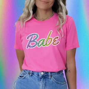 May include: Pink t-shirt with a rainbow leopard print "Babe" graphic.