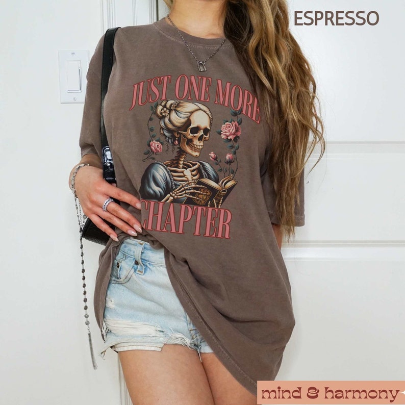 May include: A brown t-shirt with a graphic of a skeleton reading a book with the text "Just One More Chapter" printed on it.