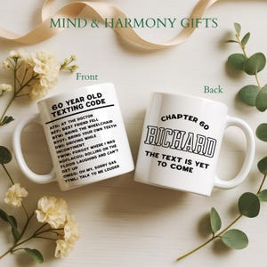May include: Two white ceramic mugs with black text. One mug reads "60 YEAR OLD TEXTING CODE" with texting acronyms. The other mug says "CHAPTER 60 RICHARD THE TEXT IS YET TO COME". The mugs are surrounded by flowers and greenery.