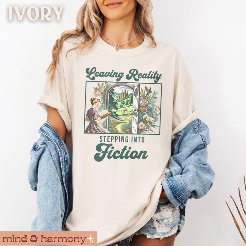May include: A white t-shirt with the text "Leaving Reality Stepping Into Fiction" in green lettering. The text is surrounded by a vintage-style illustration of a woman stepping through a doorway into a fantasy landscape.