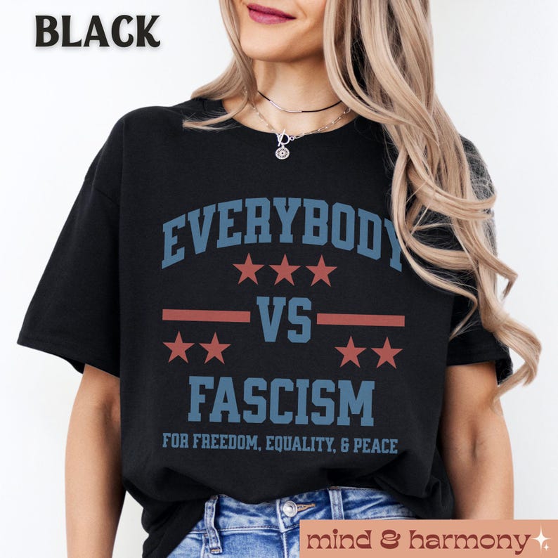 Puede incluir: Camiseta negra con el texto "EVERYBODY VS FASCISM" en letras azules y rojas. El texto est&aacute; rodeado de estrellas y una franja roja. El texto "FOR FREEDOM, EQUALITY, & PEACE" est&aacute; impreso debajo del texto principal.