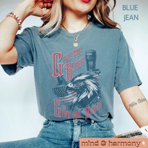 Peut inclure: Un t-shirt bleu jean avec un motif de drapeau am&eacute;ricain rouge et blanc. Le t-shirt repr&eacute;sente un aigle chauve avec un verre de bi&egrave;re et le texte "Give Me Beer Or Give Me Death".
