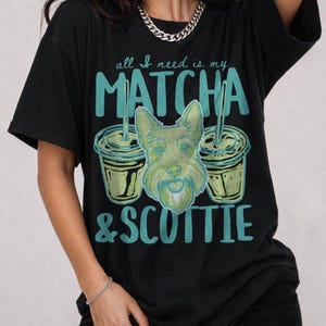 May include: Black t-shirt with the text "all I need is my MATCHA & SCOTTIE." The graphic features two matcha drinks and a green dog face. The shirt is a casual style.