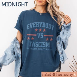 Puede incluir: Una camiseta azul marino con el texto "Everybody vs Fascism" en letras blancas y rojas. El texto est&aacute; en una fuente de estilo vintage e incluye estrellas y rayas. El texto "For Freedom, Equality, & Peace" est&aacute; impreso debajo del texto principal.