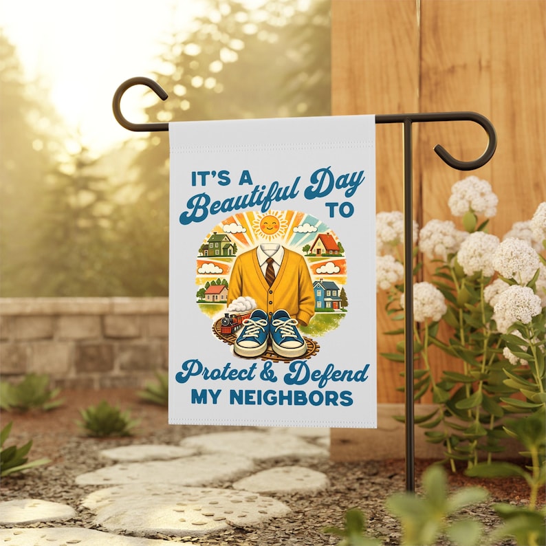May include: A white garden flag with the text "It's a Beautiful Day to Protect & Defend My Neighbors." The flag features a graphic of a person's torso wearing a yellow sweater, tie, and blue sneakers, with houses and a sun.