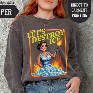 May include: A dark gray sweatshirt with the text "LET'S DESTROY ICE" and a retro illustration of a woman holding a torch over ice cubes. The sweatshirt is labeled "PEPPER" and "Comfort Colors 6014".