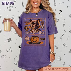 Puede incluir: Camiseta morada con un gr&aacute;fico vintage de tem&aacute;tica de Halloween que presenta un bulldog franc&eacute;s, una calabaza y el texto "Terror Bark Night: A Night of Horror, Paws & Thrills". El gr&aacute;fico tambi&eacute;n incluye el texto "Haunted Dog Houses", "Live Music", "Only 5 Bones", y "Oct 12-31".