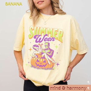 May include: A light yellow t-shirt with the text "SUMMER WEEN" in green and purple. The graphic features a couple, a bride and Frankenstein, sitting in a carved pumpkin. The shirt has a crew neck and short sleeves.