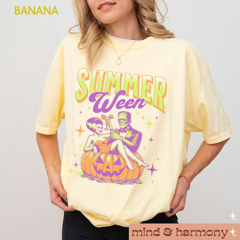 May include: A light yellow t-shirt with the text "SUMMER WEEN" in green and purple. The graphic features a couple, a bride and Frankenstein, sitting in a carved pumpkin. The shirt has a crew neck and short sleeves.