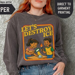May include: Pepper-colored long-sleeve shirt with a graphic that reads "LET'S DESTROY ICE." The design features cartoon children conducting a science experiment. The shirt is made of Comfort Colors material.