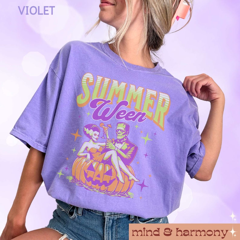 May include: Violet-colored t-shirt with the text "SUMMER Ween" in green and purple. The graphic features Frankenstein and his bride sitting on a carved pumpkin, holding cocktails. The shirt also has the text "mind & harmony".