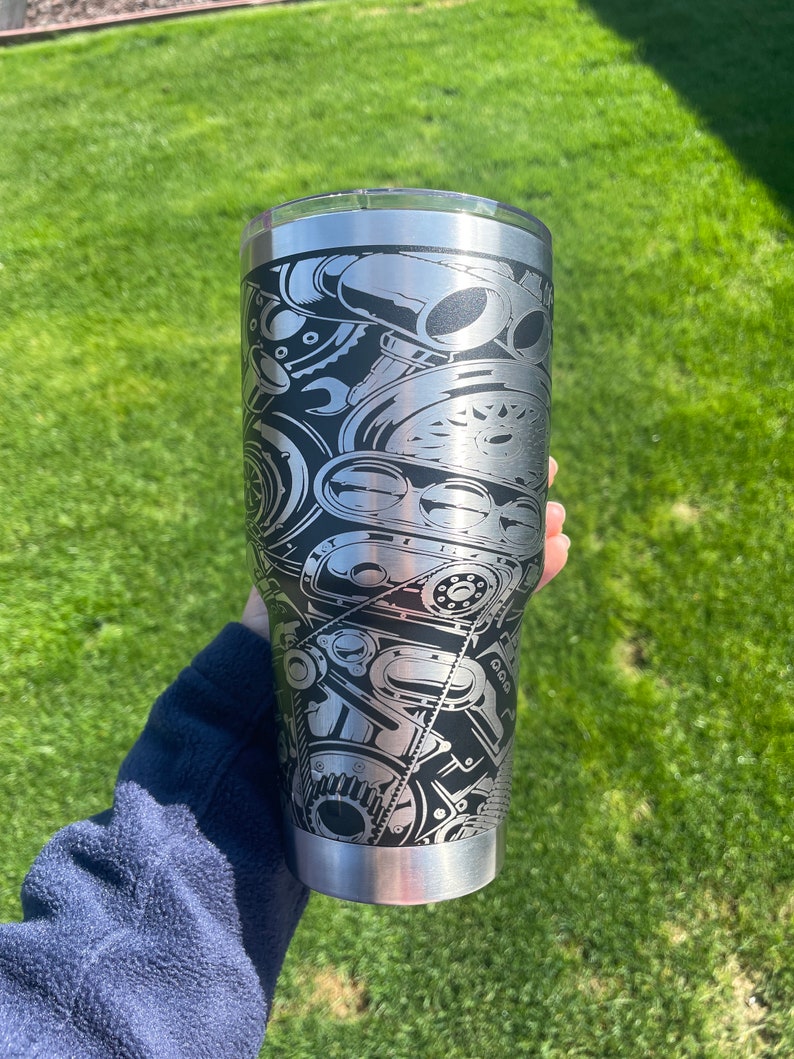 May include: A stainless steel tumbler with a black and white design of an engine. The design is detailed and intricate, featuring various engine parts.
