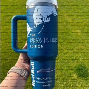 Pu&ograve; includere: Un bicchiere blu isolato con manico, con la scritta "THE SEA BLUE EDITION" e un logo Red Bull. Il bicchiere mostra anche "Juneberry" e "ENERGY DRINK" con una capacit&agrave; di 1,18 litri.