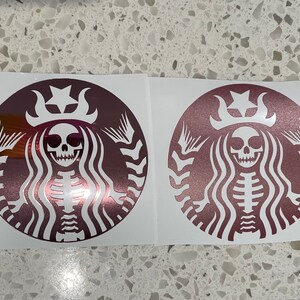 May include: Two rose gold vinyl stickers featuring a skeleton mermaid with a crown and a star on top of her head. The mermaid is in the iconic Starbucks logo shape.