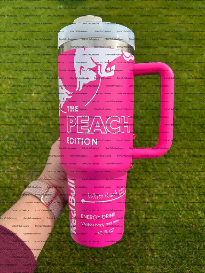 Pu&ograve; includere: Un bicchiere termico rosa con coperchio e manico bianchi. Il bicchiere presenta il testo "THE PEACH EDITION" e "White Peach ENERGY DRINK" con un logo Red Bull. Contiene 1,18 litri.