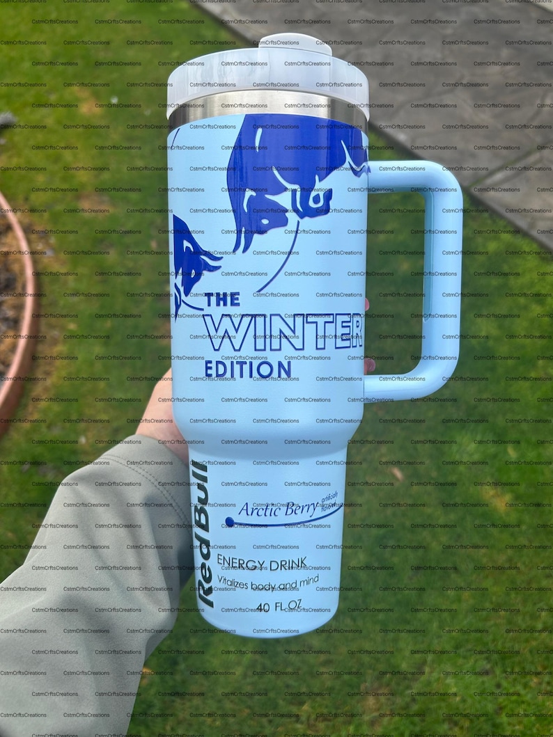 Pu&ograve; includere: Un bicchiere termico azzurro con manico, con una grafica di toro blu e la scritta "THE WINTER EDITION". Mostra anche "Red Bull Arctic Berry" e "ENERGY DRINK 40 FL OZ."