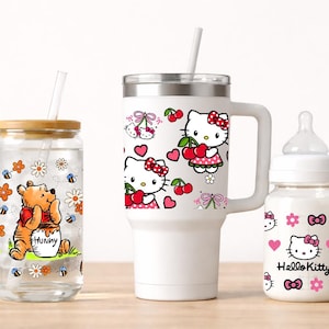 May include: A collection of drinkware featuring cartoon characters. Includes a glass with Winnie the Pooh, a white tumbler with Hello Kitty and cherries, and a baby bottle with Hello Kitty designs. Each has a straw.