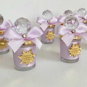 May include: Set of small glass candle jars with a purple ribbon and a crystal-like topper. Each jar has a gold sticker with the text "Bianca's Quinceañera 07.12.2024".