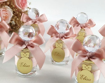 May include: Set of six small glass bottles with pink ribbon bows and crystal stoppers. Each bottle has a gold label with the name "Elisa" on it.