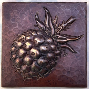 May include: A close-up of a copper tile with a raised design of a blackberry. The blackberry is made of many small, round shapes and has a stem with leaves.