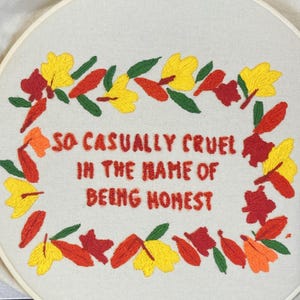 May include: Embroidered hoop art featuring a wreath of yellow and red leaves surrounding the text "So casually cruel in the name of being honest."