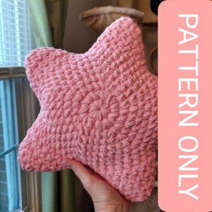 Puede incluir: Una almohada de estrella de crochet de color rosa. La almohada está hecha con un hilo esponjoso y tiene una superficie texturizada.