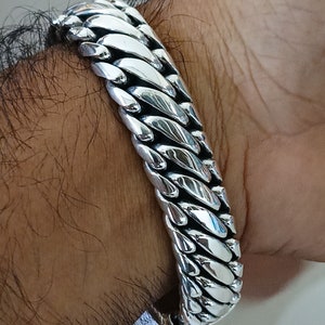 May include: A silver chain bracelet with a curb link design. The bracelet is thick and has a polished finish.
