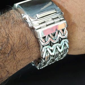 May include: A silver watch band with a unique, intricate design. The band is made of multiple interwoven links, creating a textured and stylish look.
