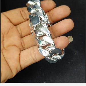 May include: A silver curb chain bracelet with a clasp closure. The bracelet is thick and chunky, with a large, bold design.