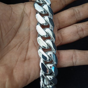 May include: A silver curb chain bracelet with a shiny finish. The chain is thick and has a large link design.