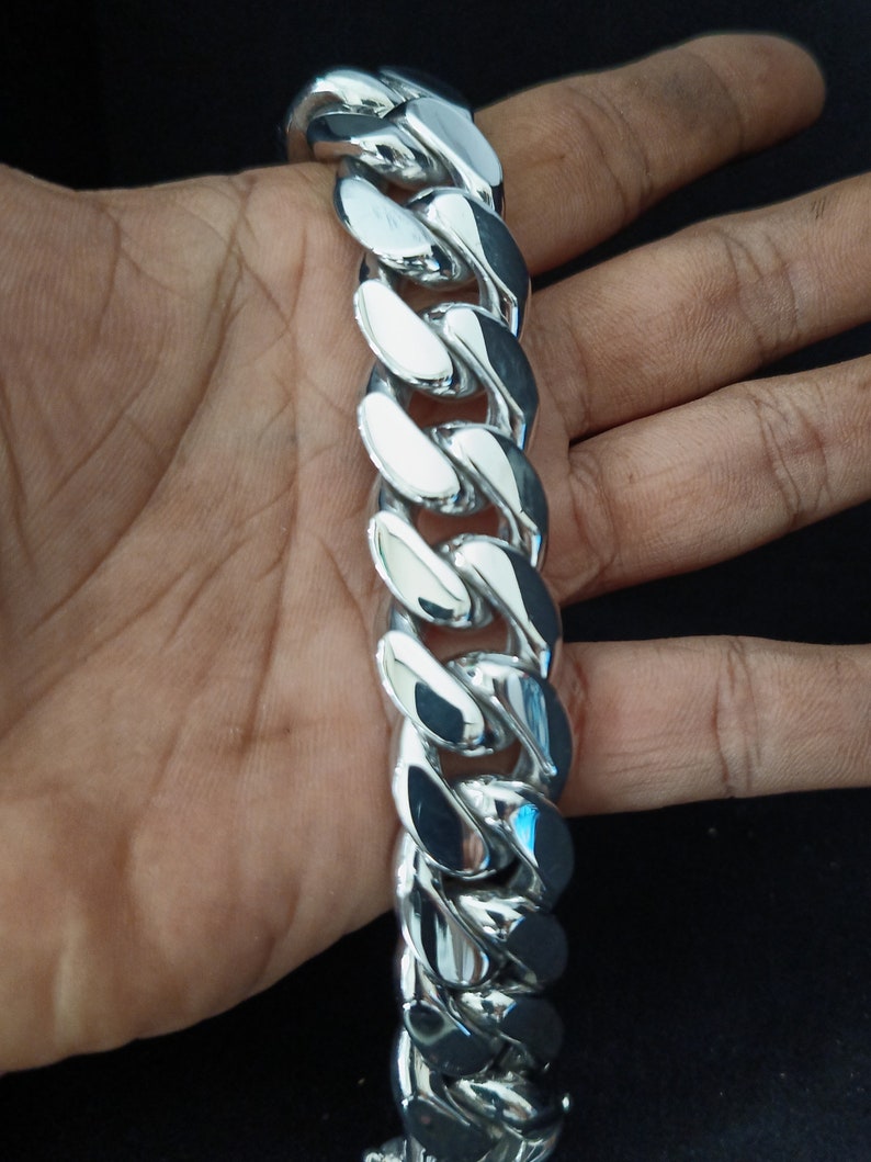 May include: A silver curb chain bracelet with a shiny finish. The chain is thick and has a large link design.