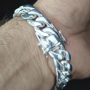 May include: A silver curb chain bracelet with a lobster clasp closure.