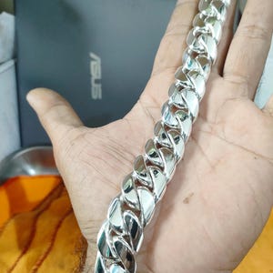May include: A silver curb chain bracelet with a clasp closure. The bracelet is thick and has a shiny finish.