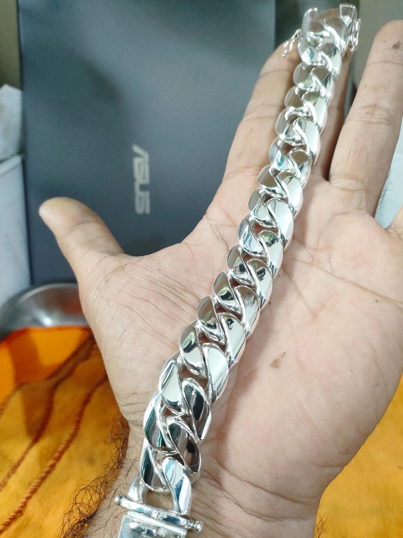 May include: A silver curb chain bracelet with a clasp closure. The bracelet is thick and has a shiny finish.