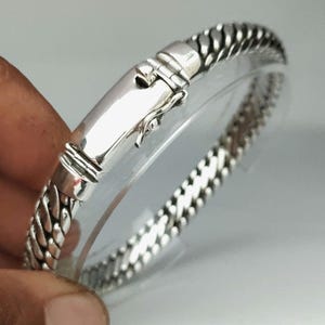 May include: A silver bracelet with a braided chain design and a clasp closure.