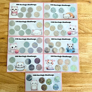 May include: Ten pink cards with a savings challenge theme. Each card features a different amount from $50 to $120, with a cute cartoon cat illustration. The cards are decorated with glitter.