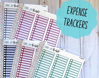 May include: A set of ten expense tracker stickers in various colors, including gold, gray, black, red, green, and blue. Each sticker has a title that reads "CARRIE JAY Budgets" and features a grid of boxes with blank spaces for writing. The stickers are designed for use in a planner or journal.