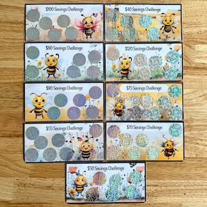 May include: Nine colorful cards with bee illustrations and glitter-covered circles. Each card features a different savings challenge amount, ranging from $40 to $120. The cards are arranged vertically on a wooden surface.