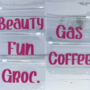 May include: Four clear plastic zippered pouches with pink lettering. The pouches are labeled "Beauty", "Fun", "Gas", and "Coffee".
