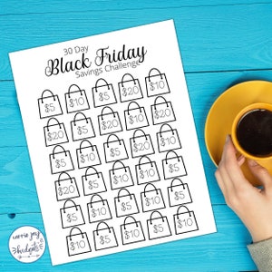 Puede incluir: Un papel blanco con un dise&ntilde;o de bolsa de la compra en negro para un desaf&iacute;o de ahorro del Black Friday de 30 d&iacute;as. Las bolsas est&aacute;n etiquetadas con cantidades de 5 &euro; a 20 &euro;. Una taza de caf&eacute; amarilla est&aacute; sobre una superficie de madera azul.