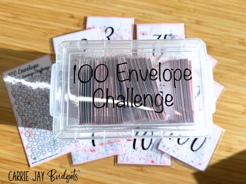 May include: A clear plastic container with a lid, filled with envelopes. The container has a black label that reads "100 Envelope Challenge". The container is surrounded by envelopes with numbers written on them.