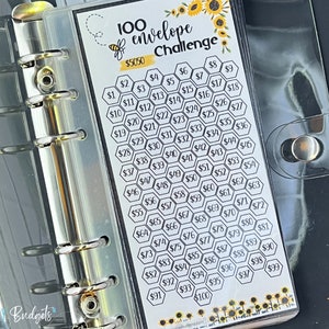 May include: A 100 envelope challenge budget planner with a bee and sunflower design. The planner is in a clear plastic binder with silver rings. The planner has a honeycomb pattern with numbers 1 through 100 in black text. The planner is labeled "100 envelope challenge" and "$5050".