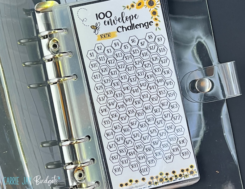May include: A 100 envelope challenge budget planner with a bee and sunflower design. The planner is in a clear plastic binder with silver rings. The planner has a honeycomb pattern with numbers 1 through 100 in black text. The planner is labeled "100 envelope challenge" and "$5050".