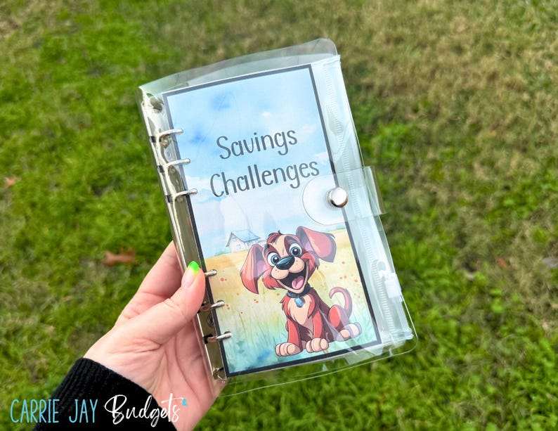 Puede incluir: Un archivador de pl&aacute;stico transparente con una cubierta colorida que presenta un perro de dibujos animados y el texto "Savings Challenges".